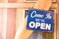 Ã¢â¬ÅCome in weÃ¢â¬â¢re open Ã¢â¬Å metal label Hang on a wooden door at a restaurant . vintage tone Royalty Free Stock Photo